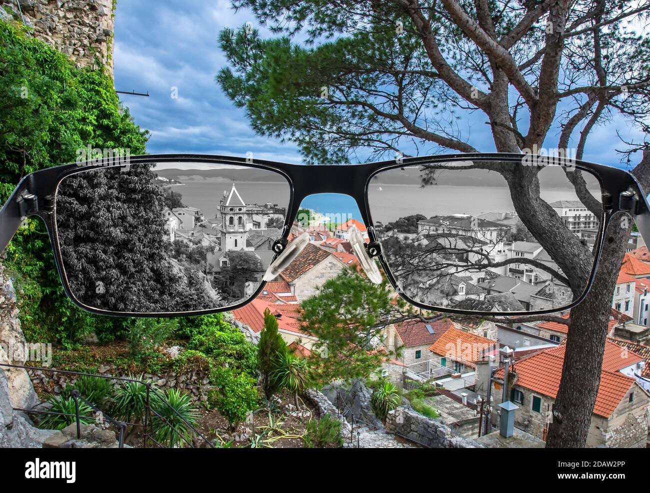 Looking through glasses to desaturated view of pine tree,  old city center with rooftops and see. Color blindness. World perception during depression. Stock Photo