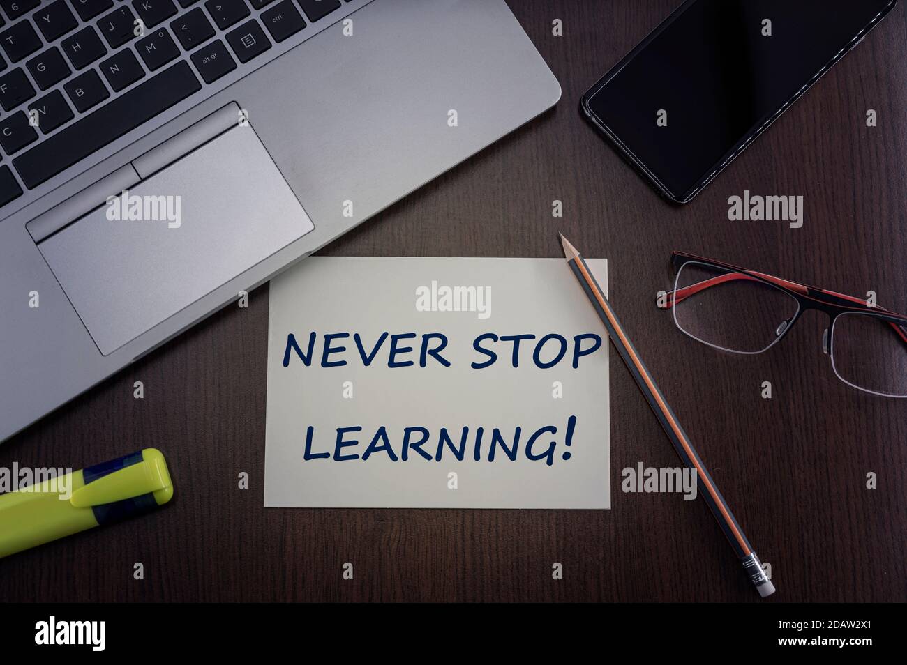 Learning concept. Top view of laptop, phone, glasses and pencil with card with inscription never stop learning. Stock Photo