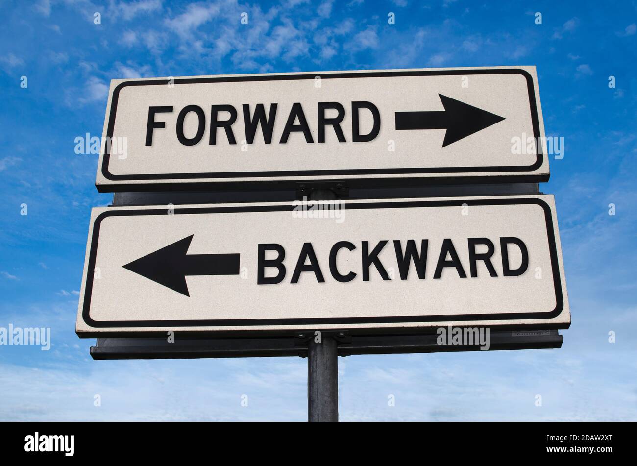 Forward vs backward. White two street signs with arrow on metal pole with word. Directional road. Crossroads Road Sign, Two Arrow. Blue sky background Stock Photo