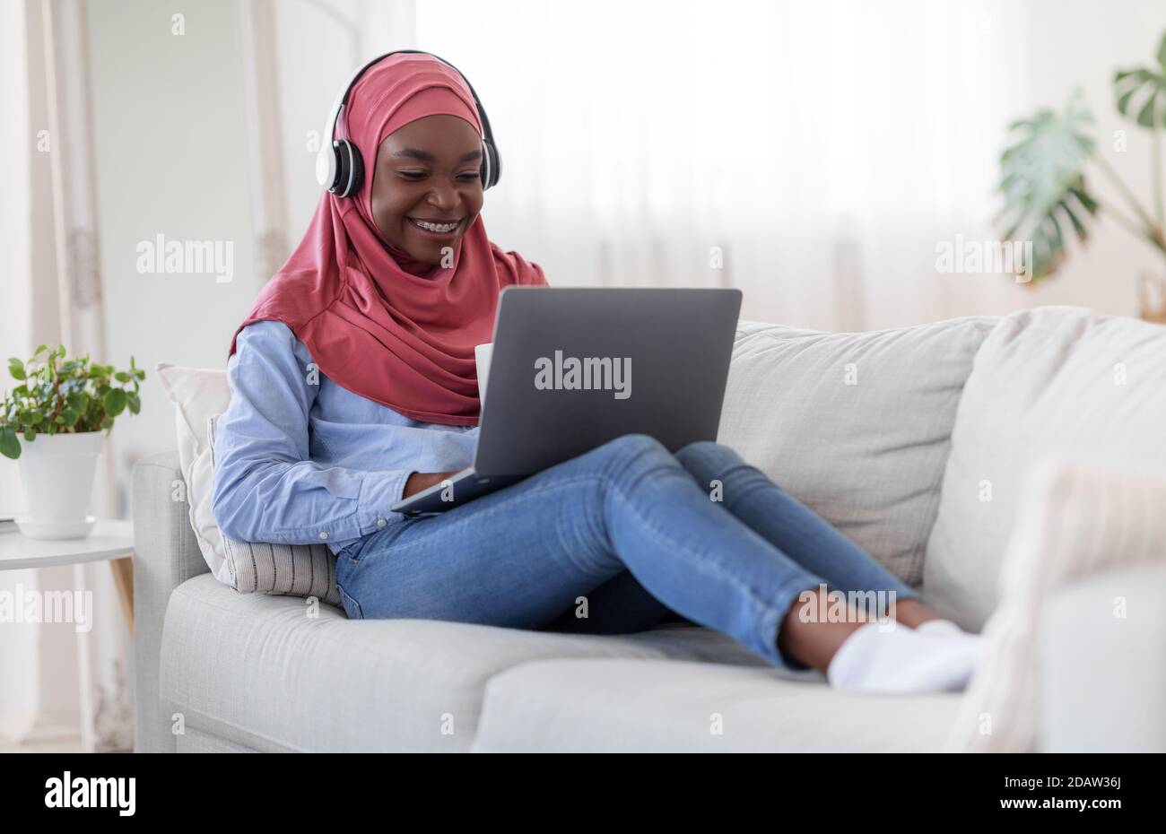 Enjoying time at home. Black muslim woman using laptop and drinking ...