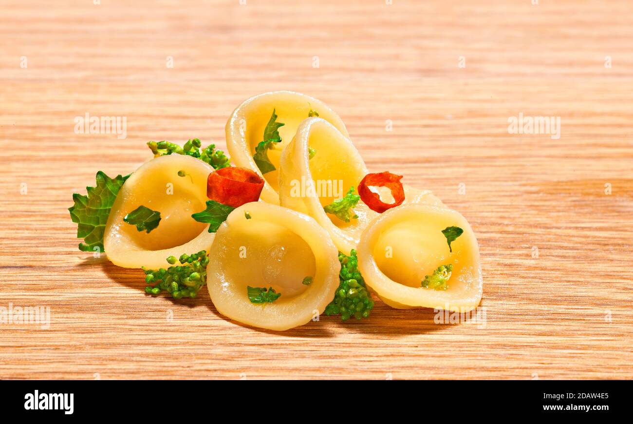 Orecchiette pasta, with turnip tops and chilli, on a wooden base. Stock Photo