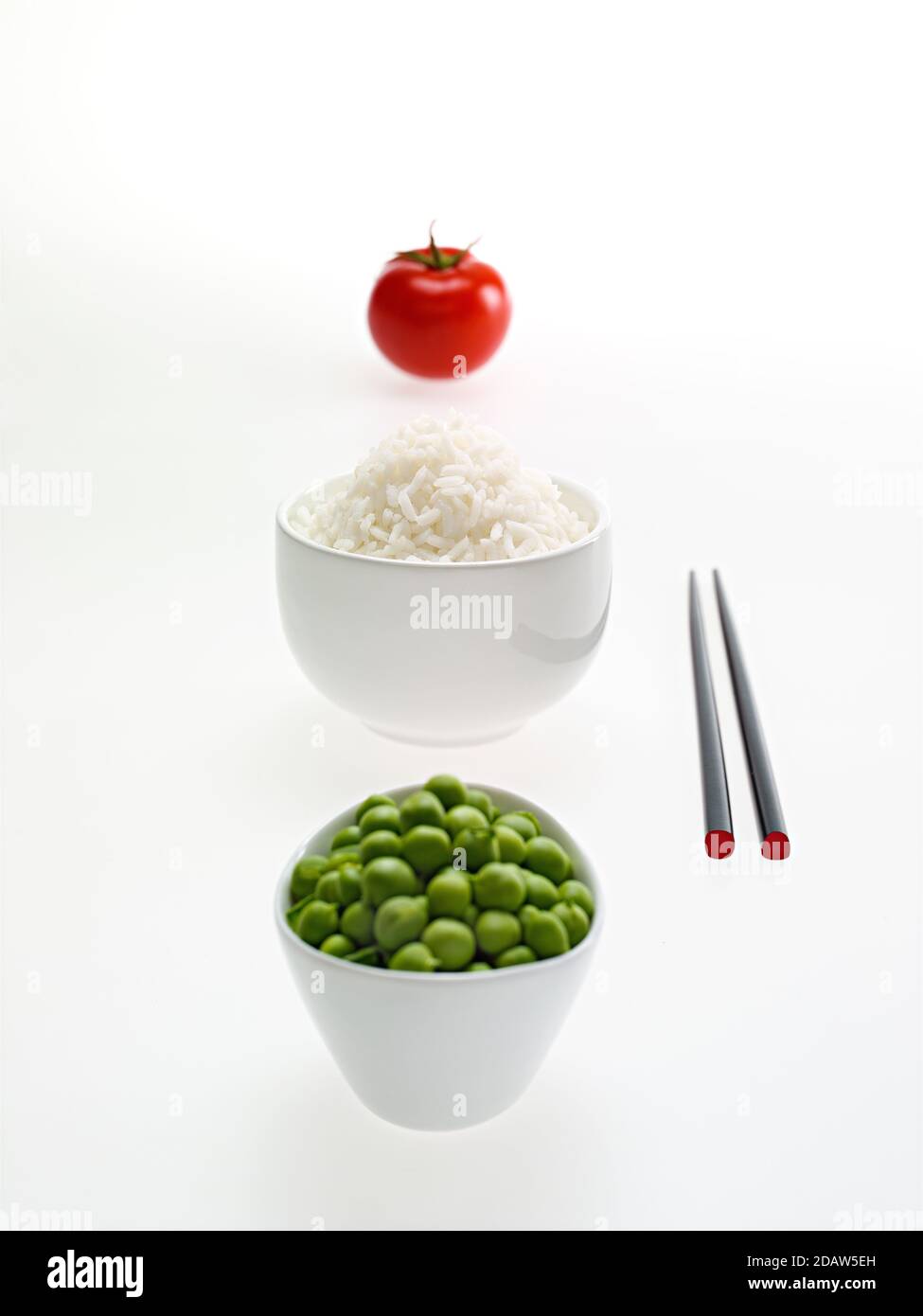 Tomato, rice and peas, with white bowls, and Chinese chopsticks, over white background. Stock Photo