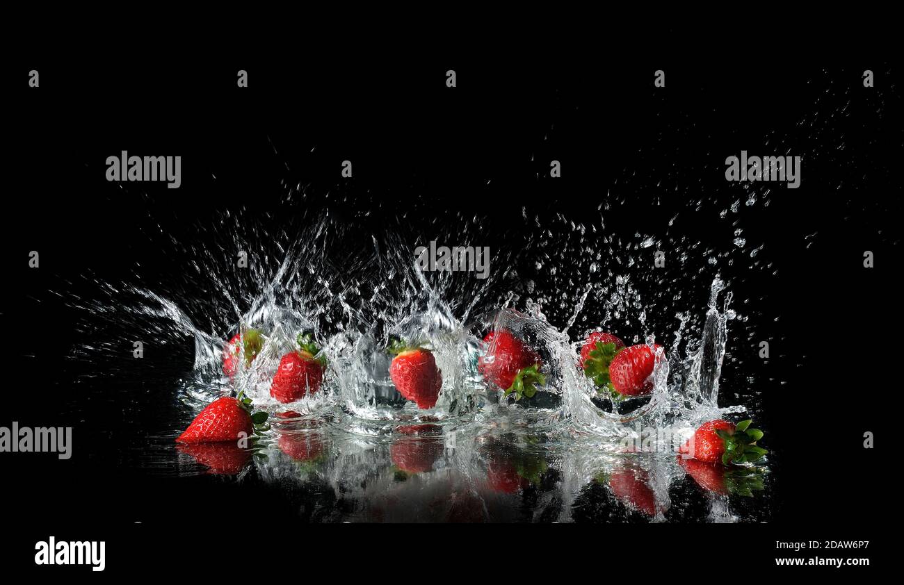 Group of falling strawberries with splashing water on black background ...