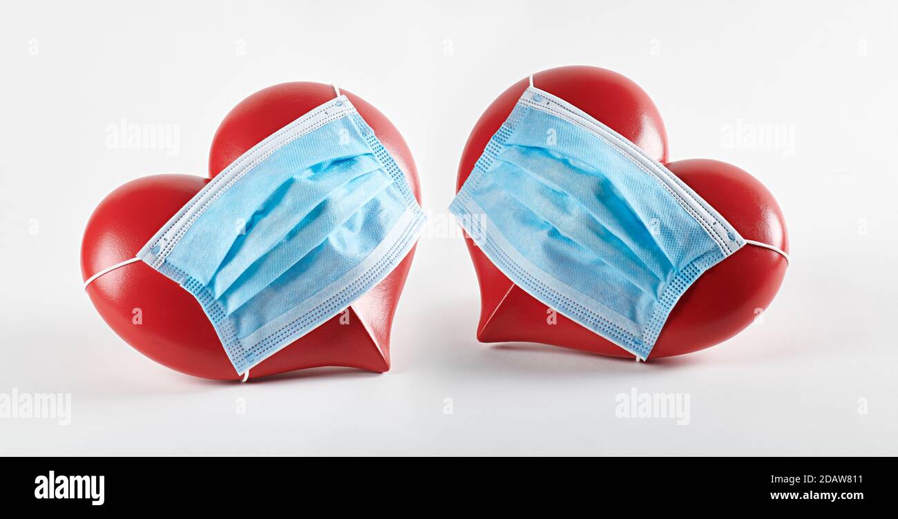 Two red hearts wearing covid mask, on white background, with shadows. Stock Photo