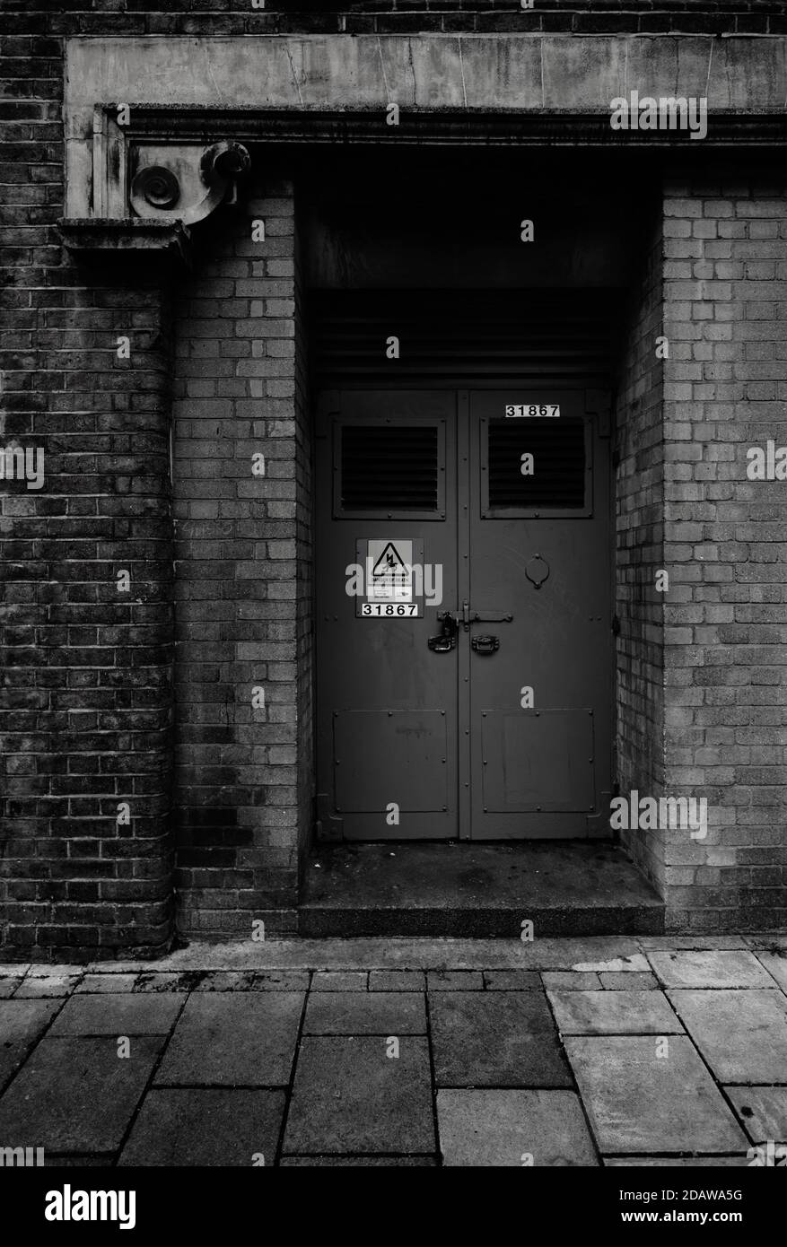 Black and white monochrome image of blue works or engineering door to old brick building Stock Photo