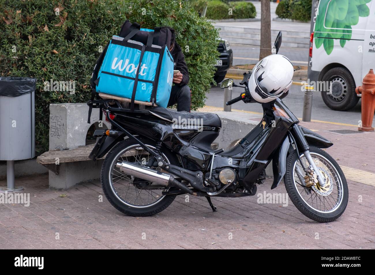 Athens, Greece. November 12, 2020. Wolt food delivery service, courier sitting next to the parked scooter in the city center street Stock Photo