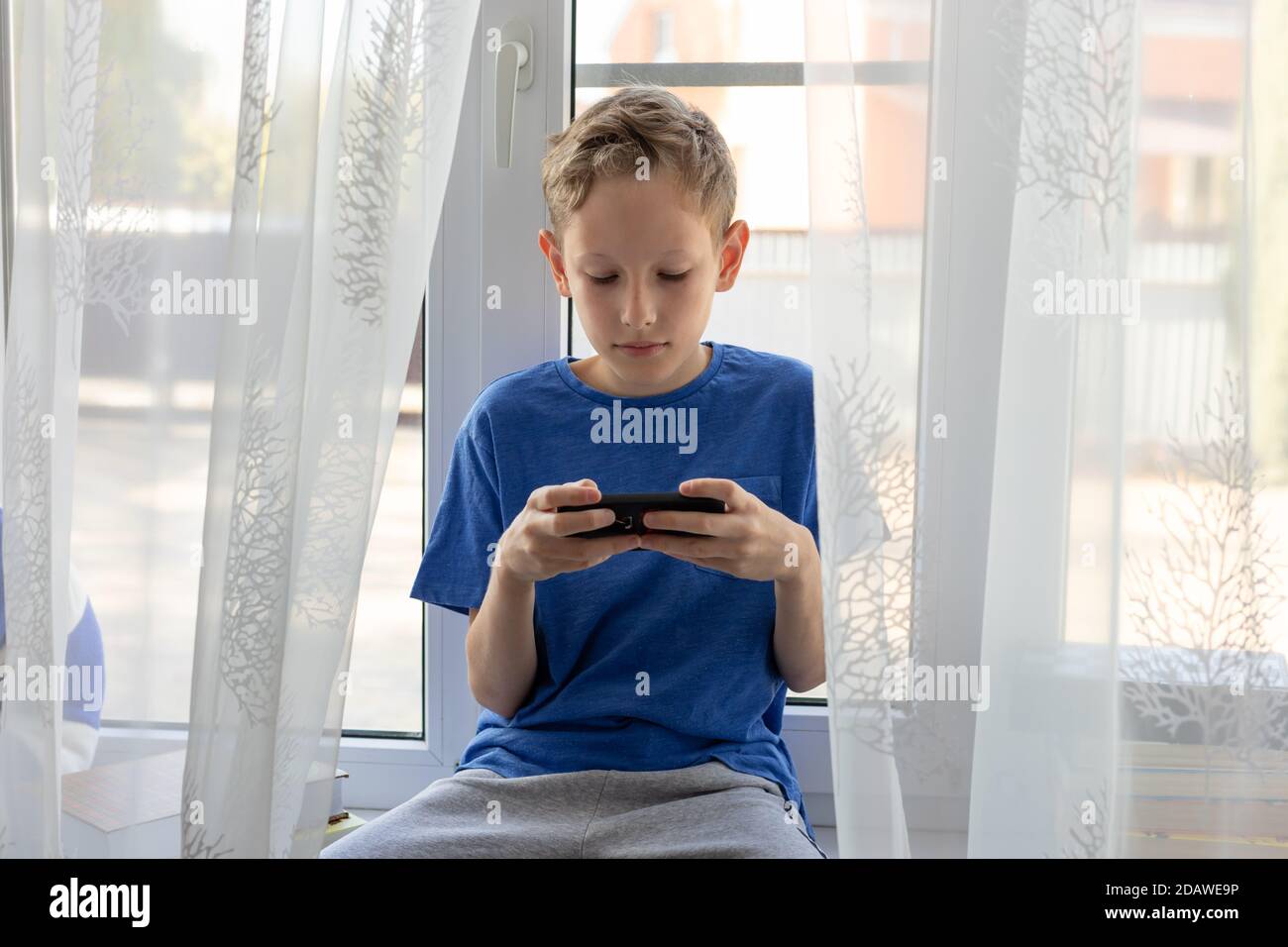 Preteen boy uses mobile phone, looking at the screen, playing, using apps. Stock Photo