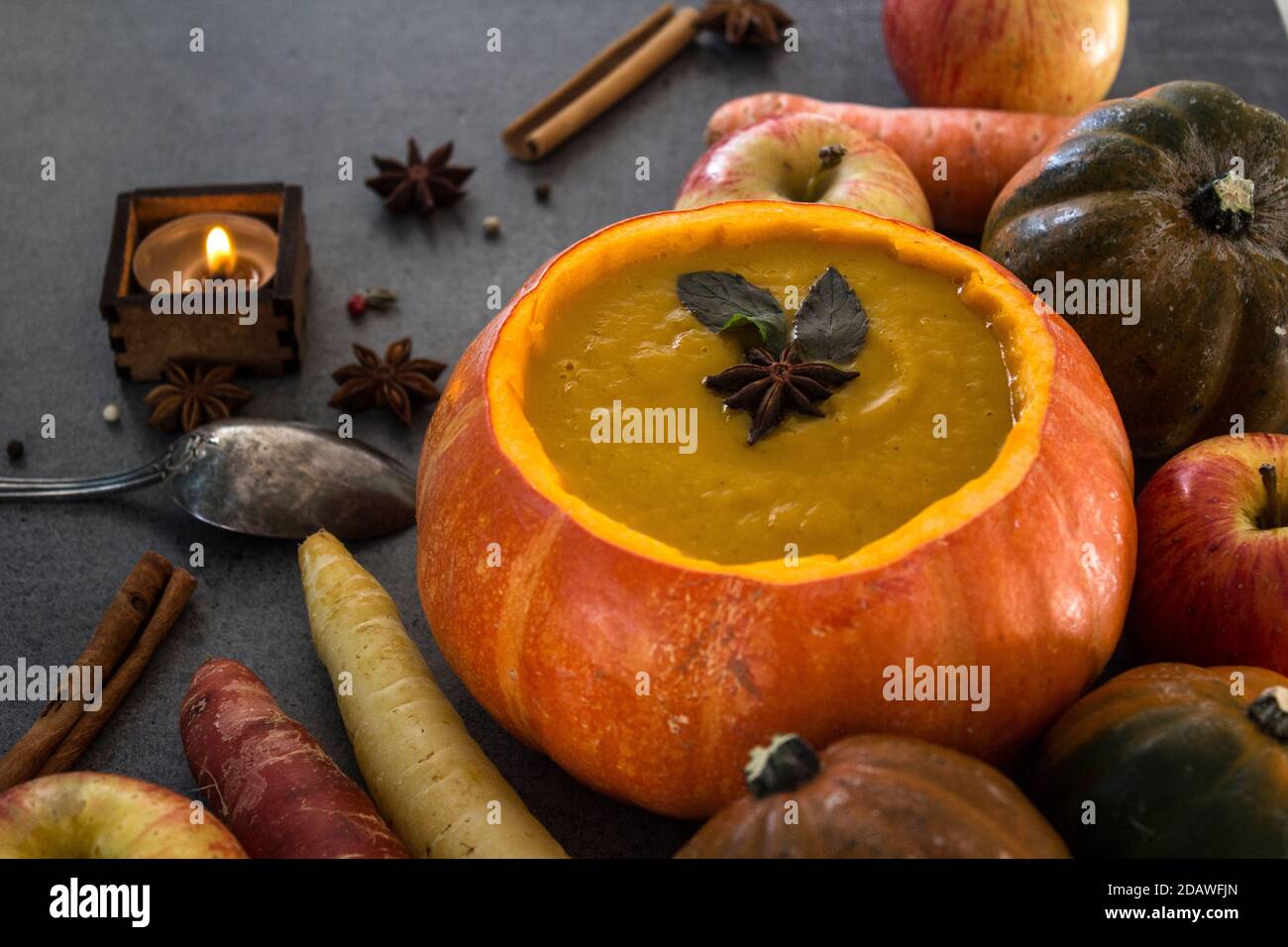 Squash soup in pumpkin bowl. Top view photo of pumpkin, apples, carrots anise stars and cinnamon sticks. Grey background. Stock Photo
