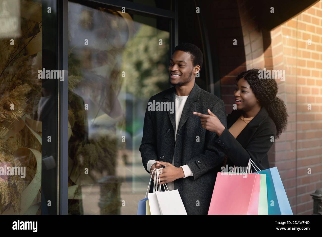 Cool sale in brand store, i want it. Interested african american guy and lady with colored paper bags walking to street Stock Photo