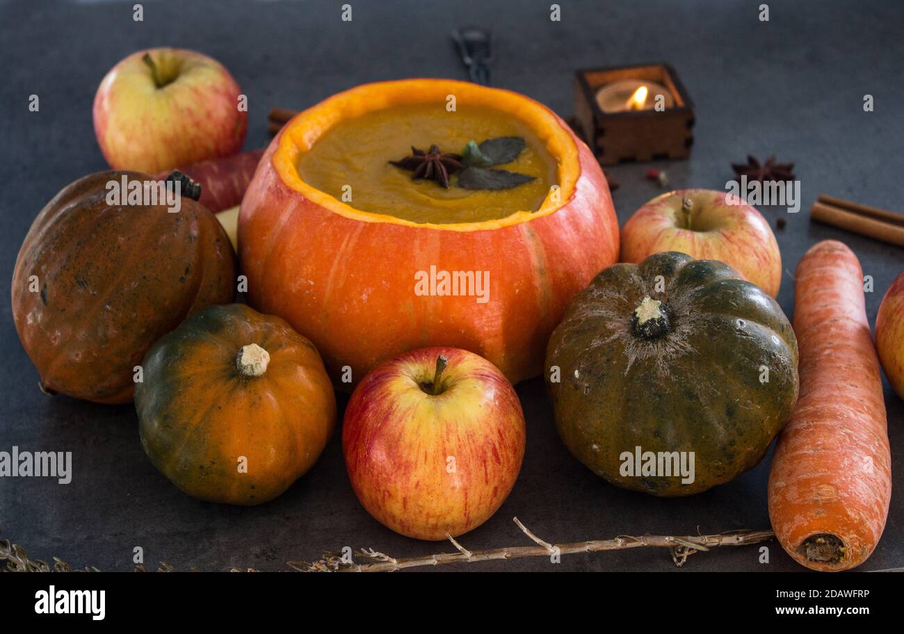 Squash soup in pumpkin bowl. Top view photo of pumpkin, apples, carrots anise stars and cinnamon sticks. Grey background. Stock Photo