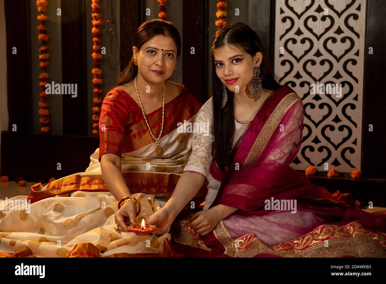 An Indian mother and daughter celebrating the Festival of Lights by lighting candles and diyas at home, Indian family celebrating Diwali. Stock Photo