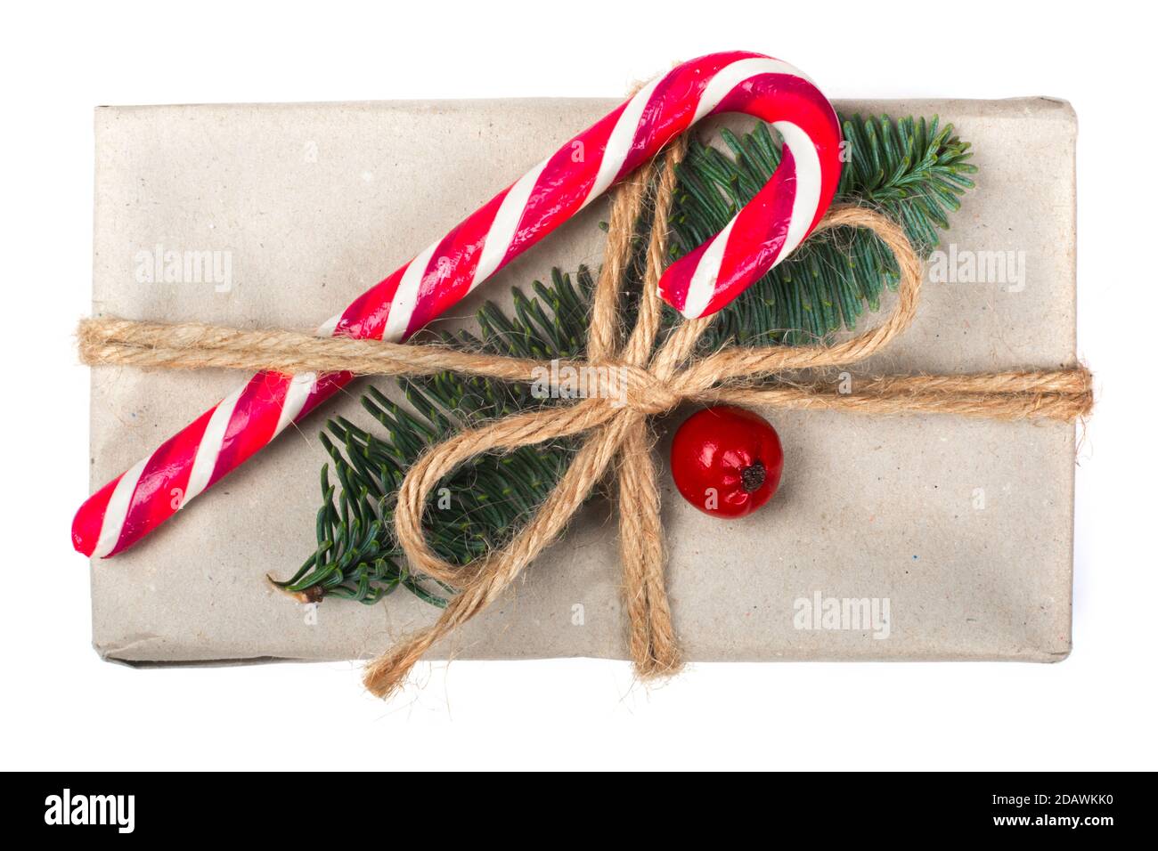 Wrapped vintage christmas gift box in craft paper with rope bow, striped candy cane fir tree twig and red berry isolated on white Stock Photo