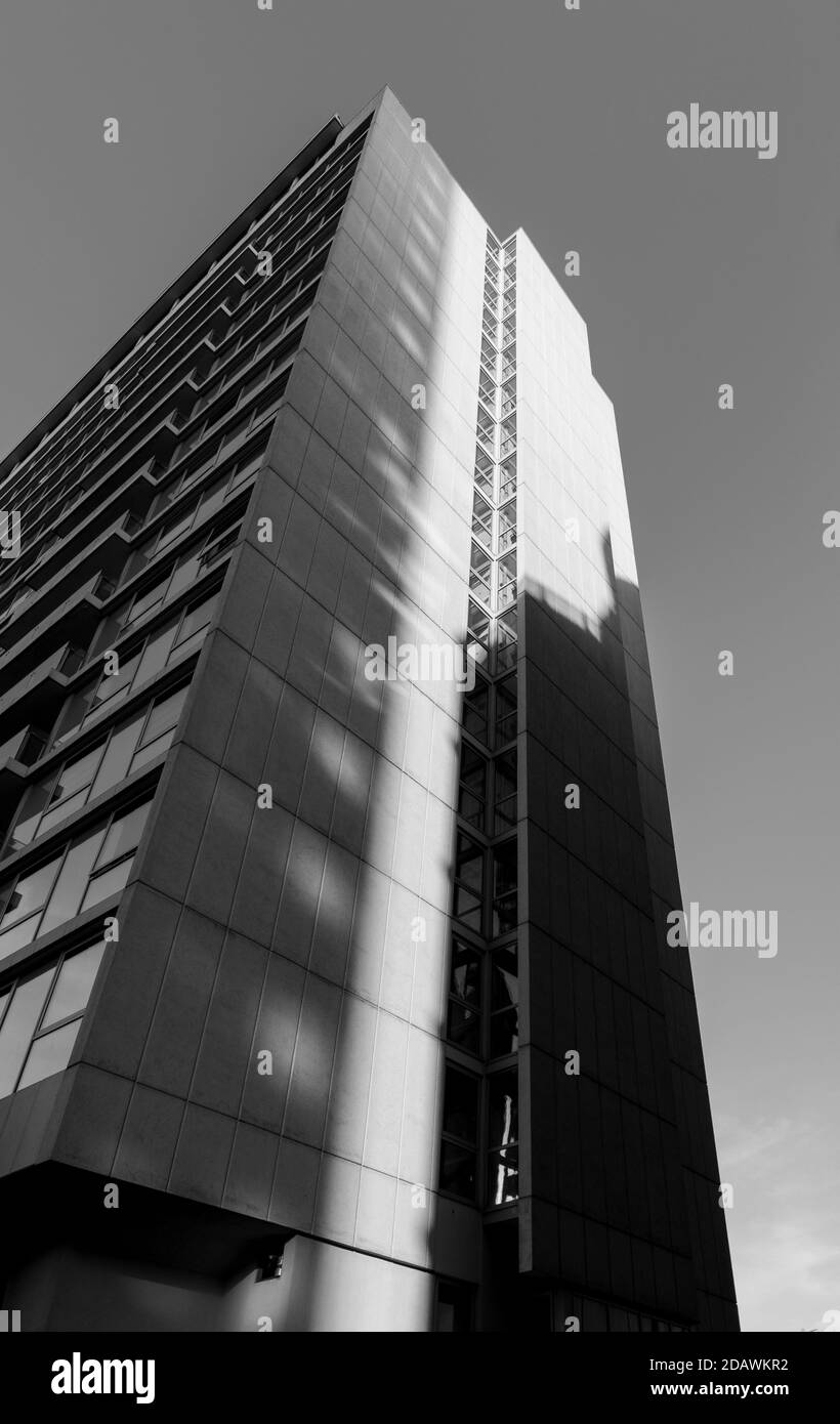 Black and white monochrome image looking up at a tall apartment building on a clear sunny day with vertical shadows cast across Stock Photo