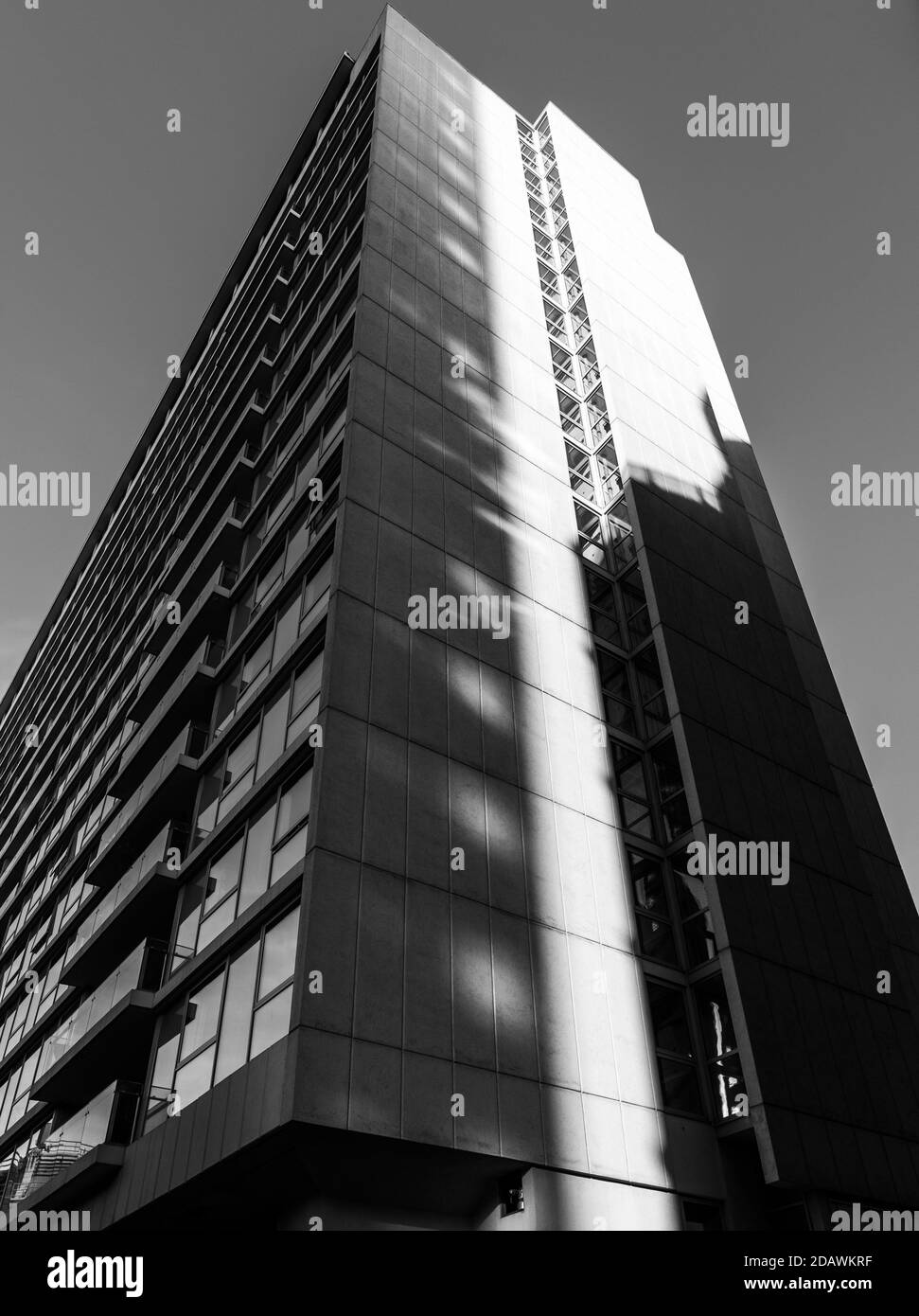 Black and white monochrome image looking up at a tall apartment building on a clear sunny day with vertical shadows cast across Stock Photo