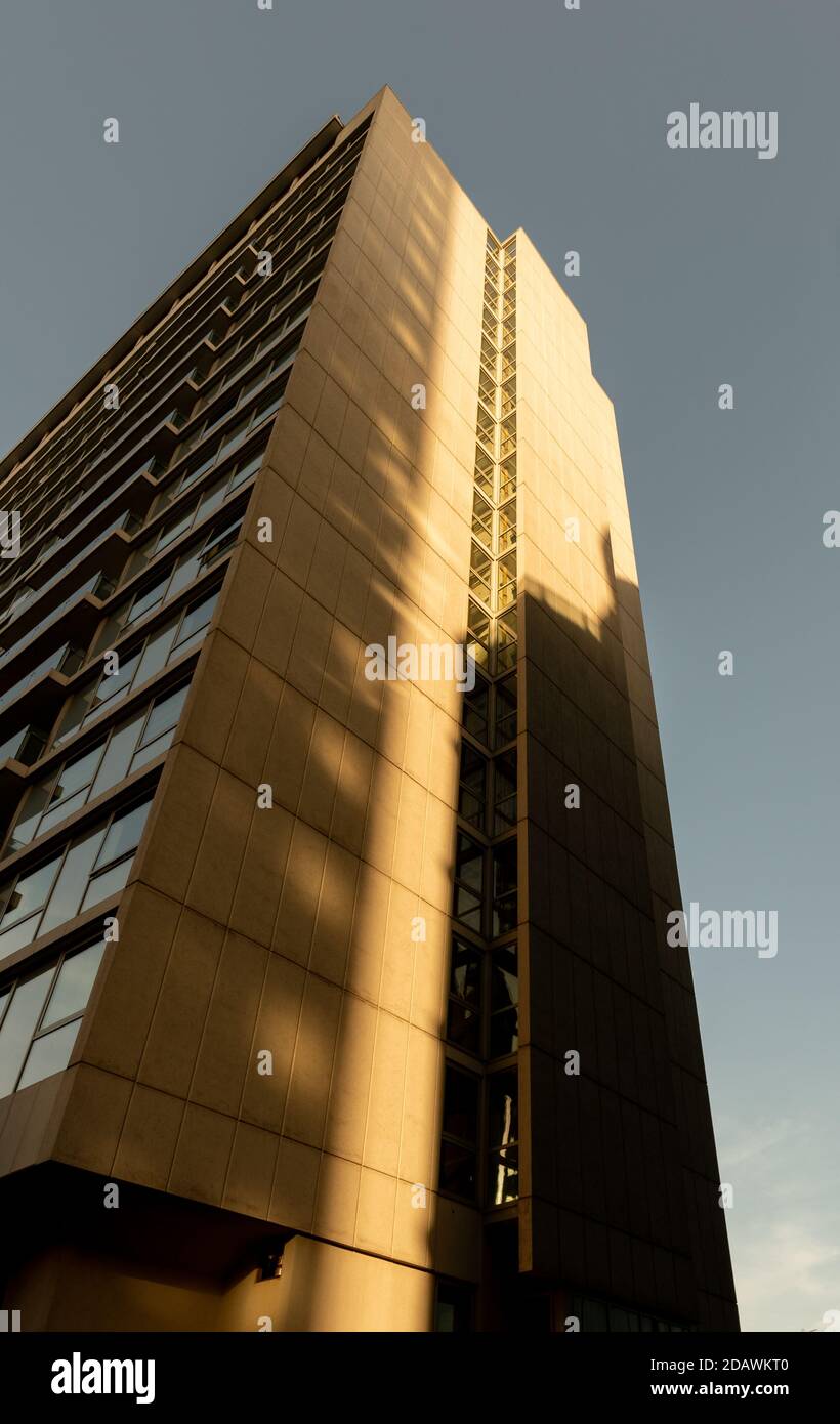 Looking up at a tall apartment building on a clear sunny day with vertical shadows cast across Stock Photo