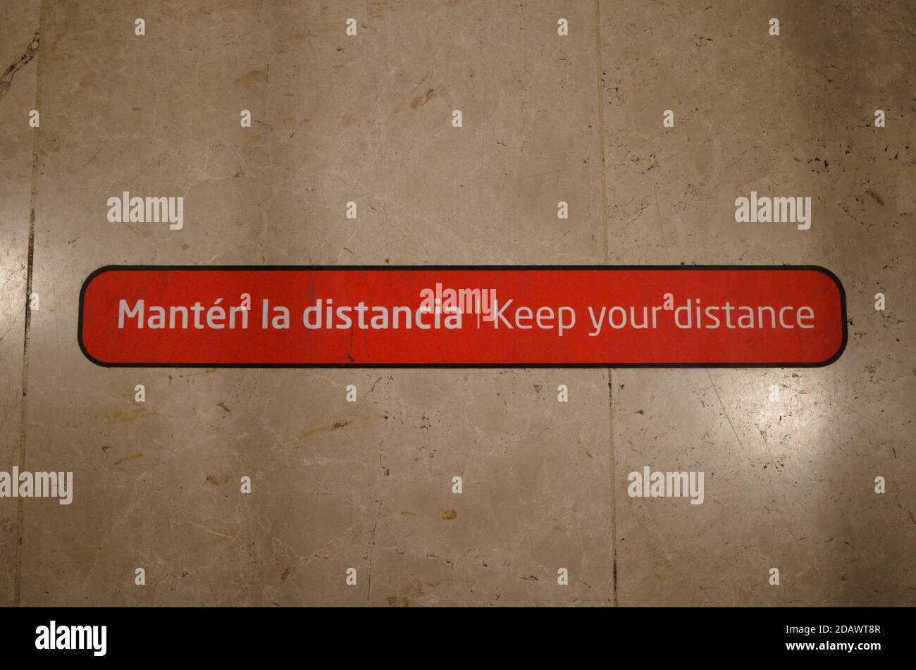 Keep your distance warning message on the floor of international airport during pandemic written in Spanish and English languages. Stock Photo