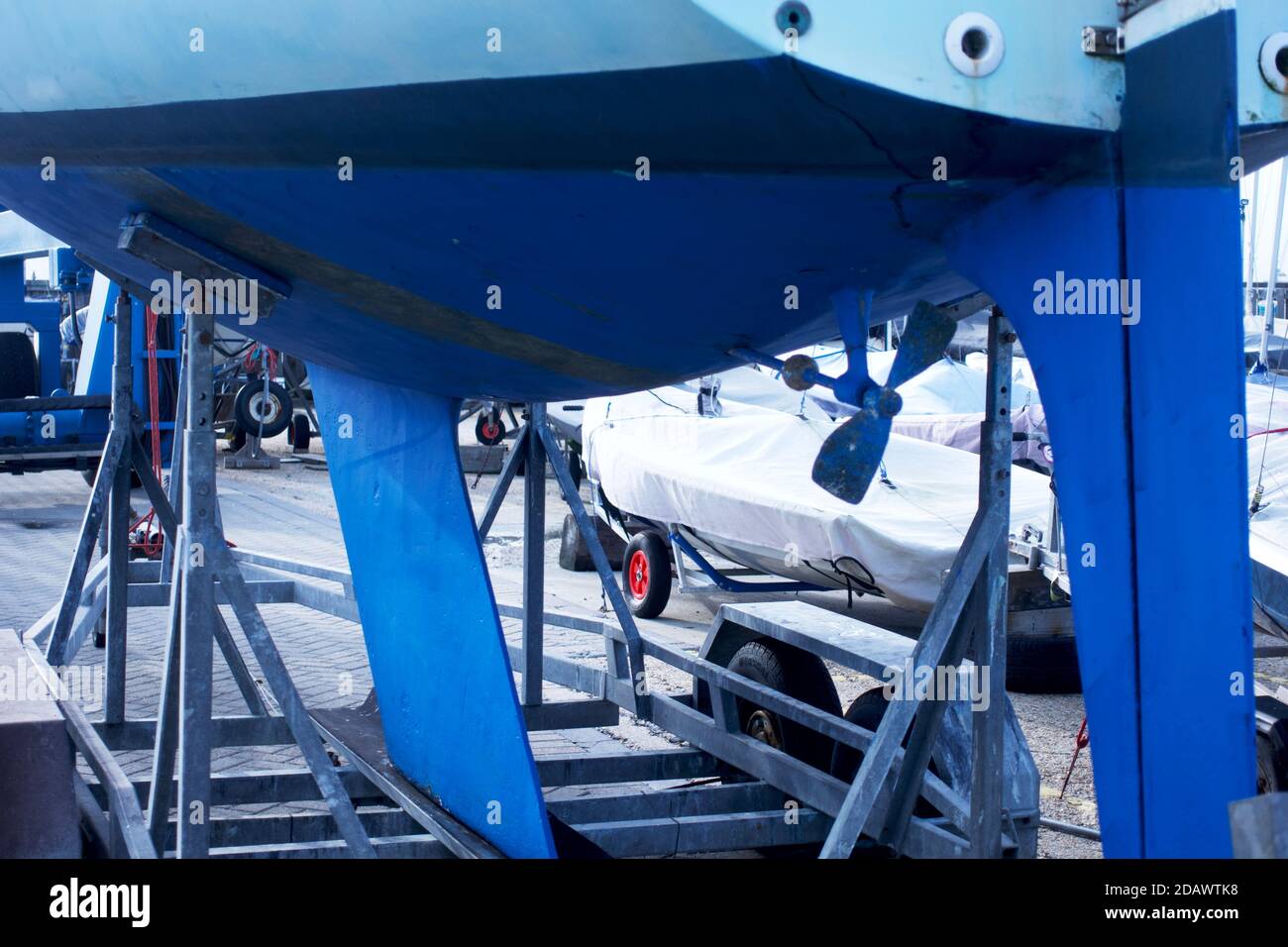 A sailing yacht or boat on the hard in a boatyard, with hull showing a blue coloured anti-fouling layer to slow the growth of subaquatic organisms. Stock Photo