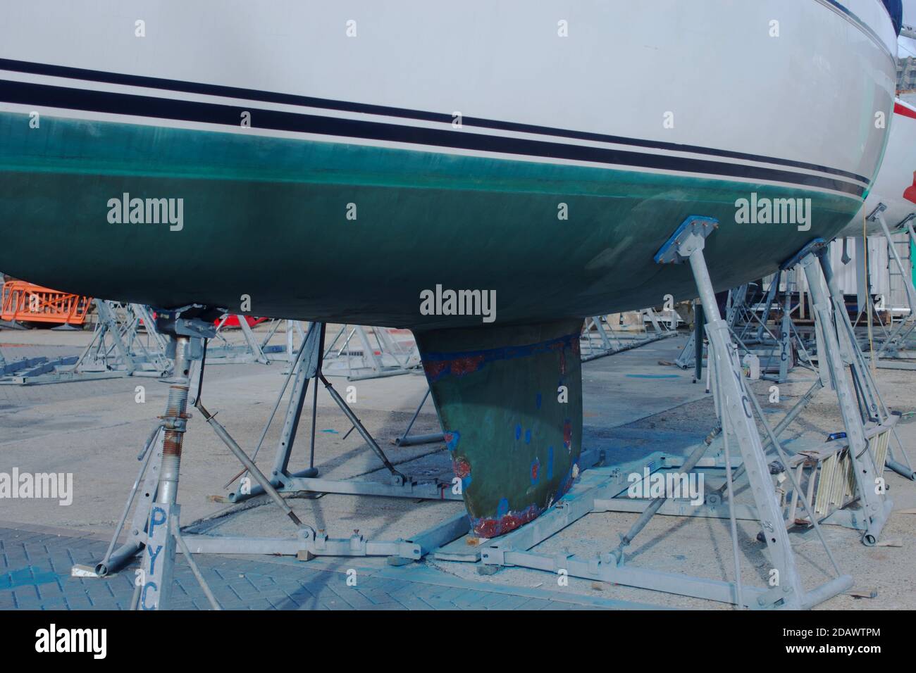 A sailing yacht or boat on the hard in a boatyard, with hull showing a green coloured anti-fouling layer to slow the growth of subaquatic organisms. Stock Photo
