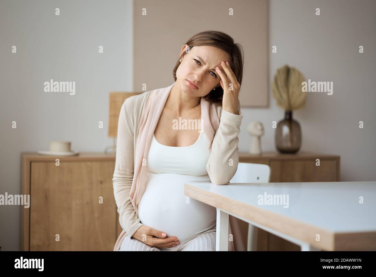 Pregnant woman suffering from headaches while sitting at the table Stock Photo