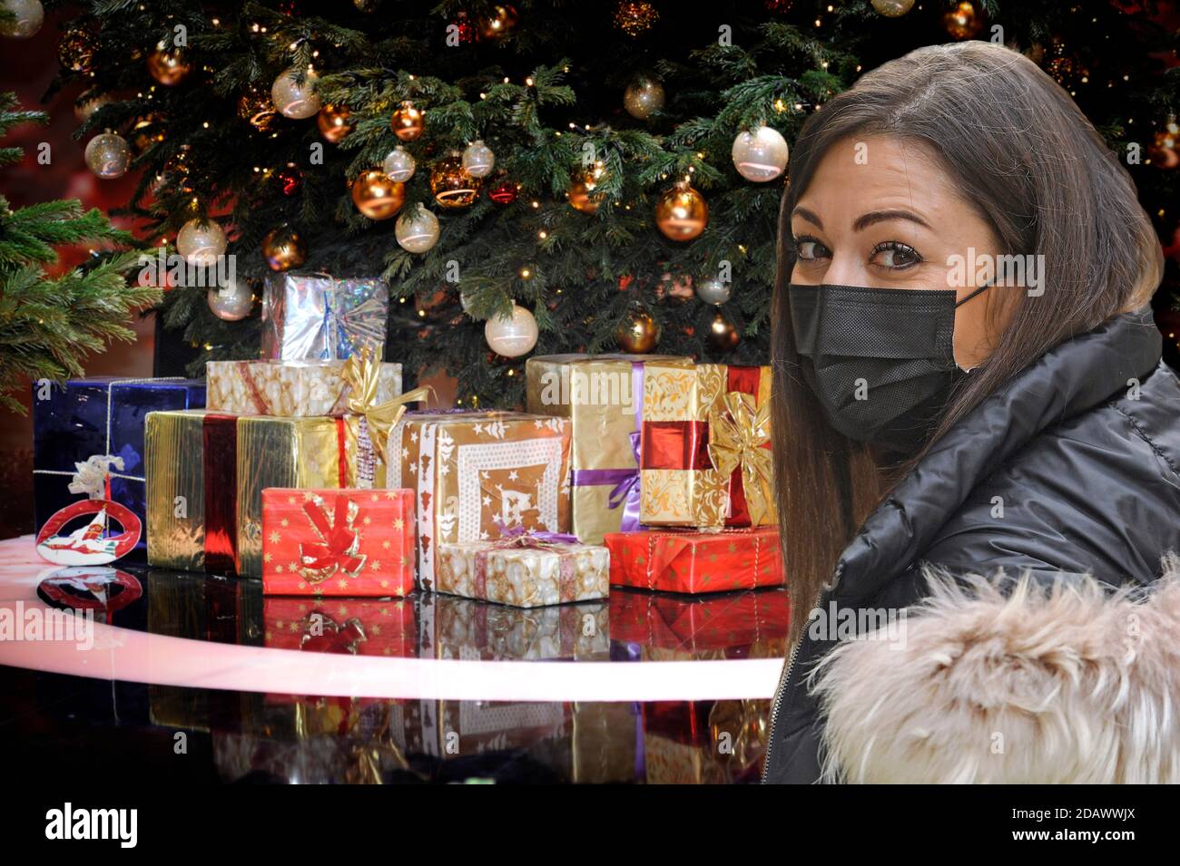FOTOMONTAGE-Weihafterten 2020 in the middle of the coronavirus pandemic. What about the partial lockdown? Loosening of detainees will probably only be done with significantly decreasing corona numbers. Young woman with face mask, mask in front of Weihaftertsbaum, Weihaftertsbaum, Christmas tree, Christmas tree, Christmas tree, decorated, Christmas tree ball. Gifts, packages. | usage worldwide Stock Photo