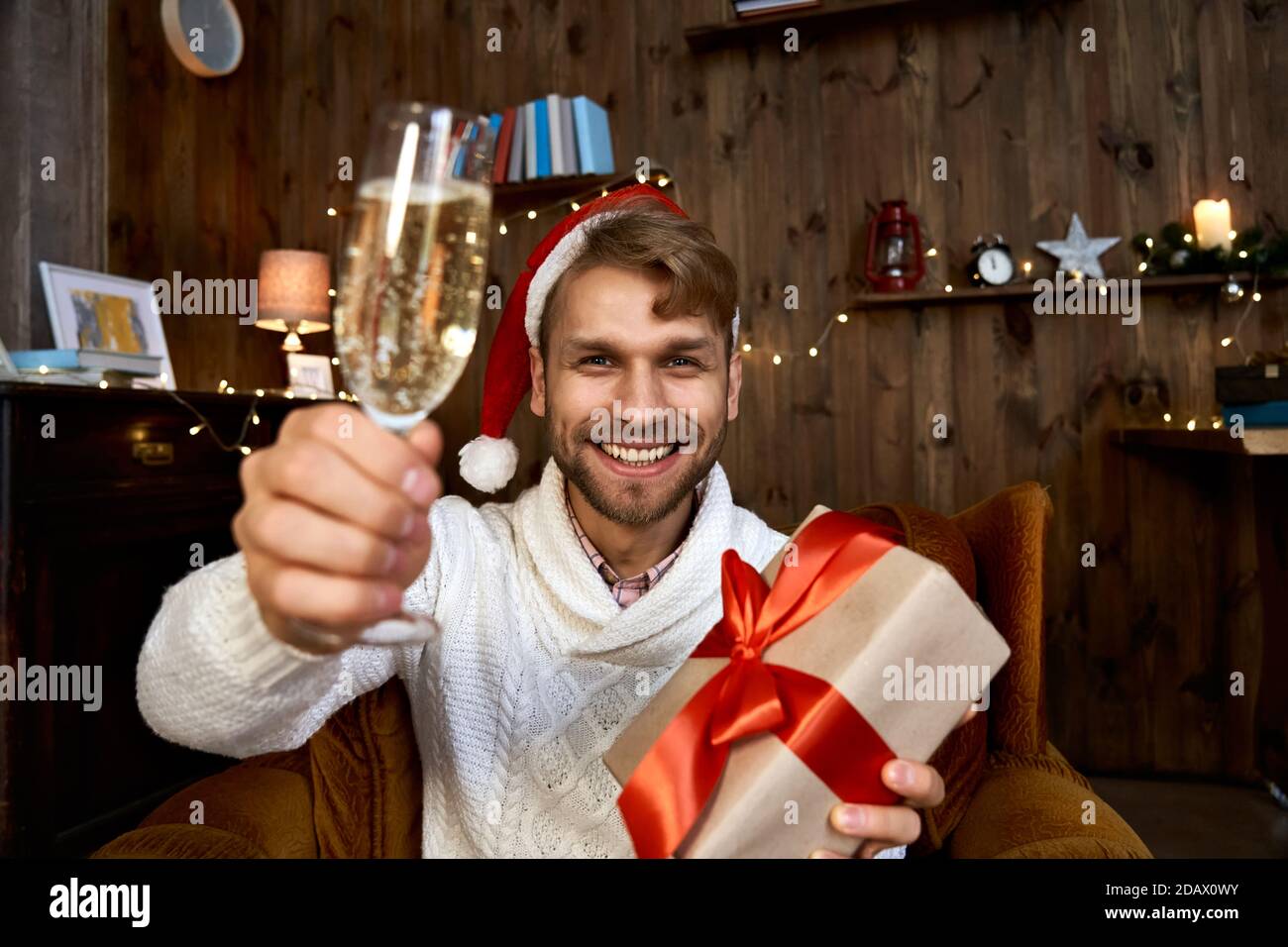 Happy man wearing santa hat holding Christmas gift looking at camera. Stock Photo