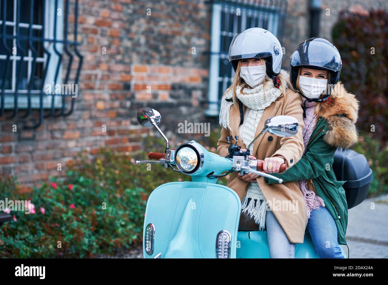 Two women wearing masks and commuting on scooter Stock Photo