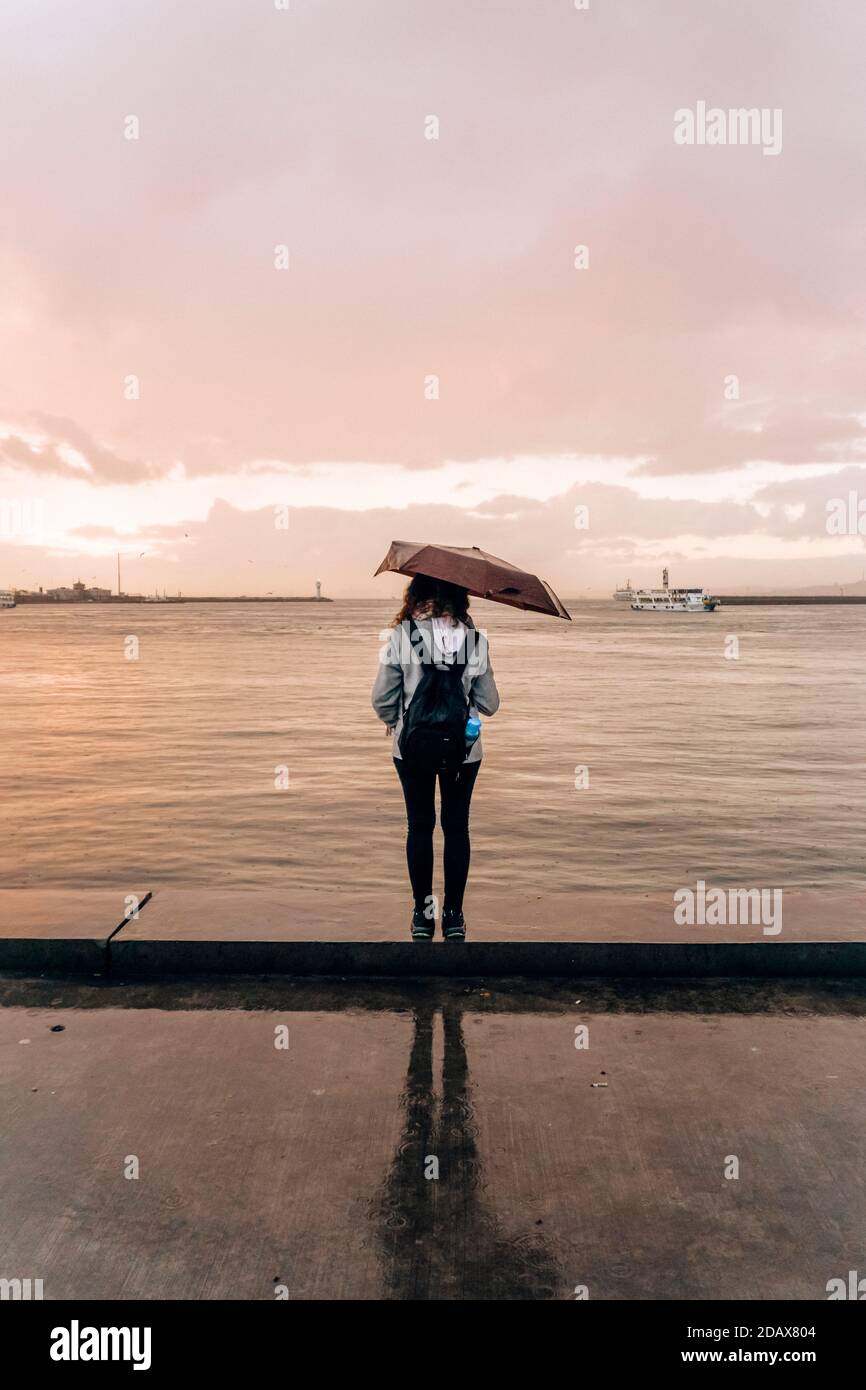 Lonely girl in the rain with an umbrella at the sea pier. Sad girl ...