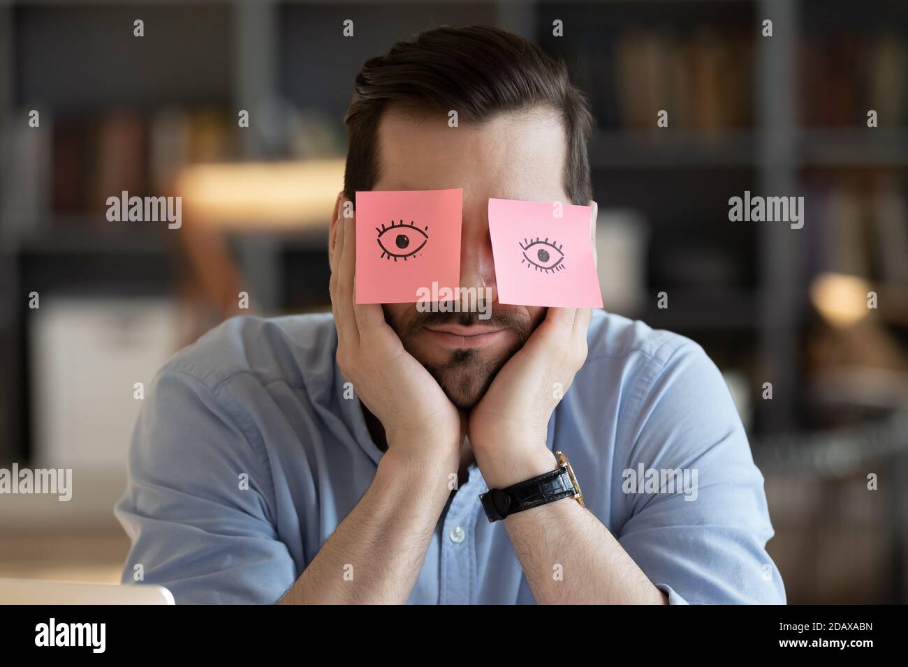 Employee hides eyes with sticky notes wants sleep at workplace Stock Photo