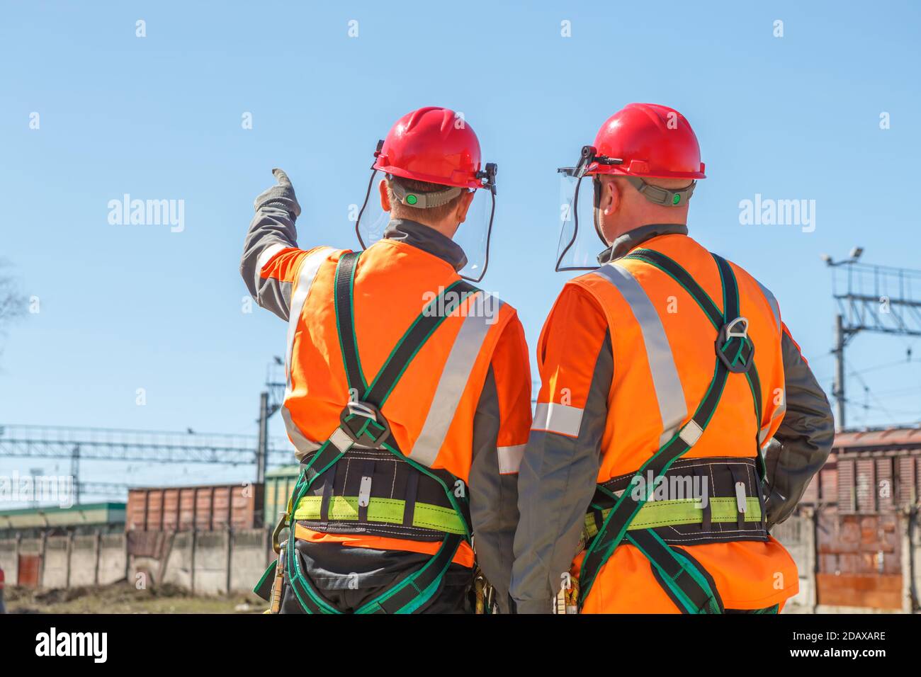 Two working electricians look at the high voltage power lines and railway cars shows his hand Stock Photo