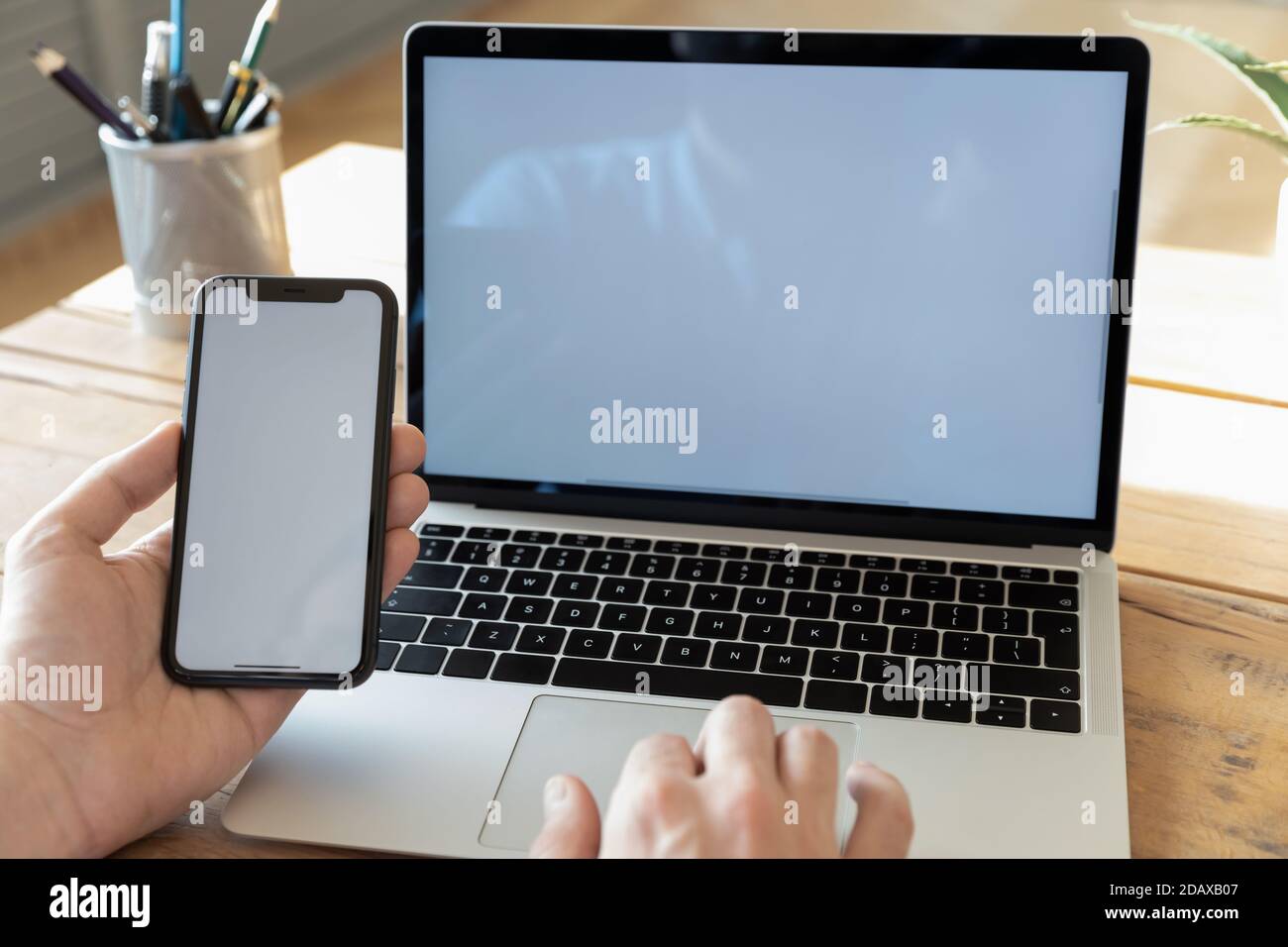 Man using computer holding smartphone with white empty mockup screen Stock Photo