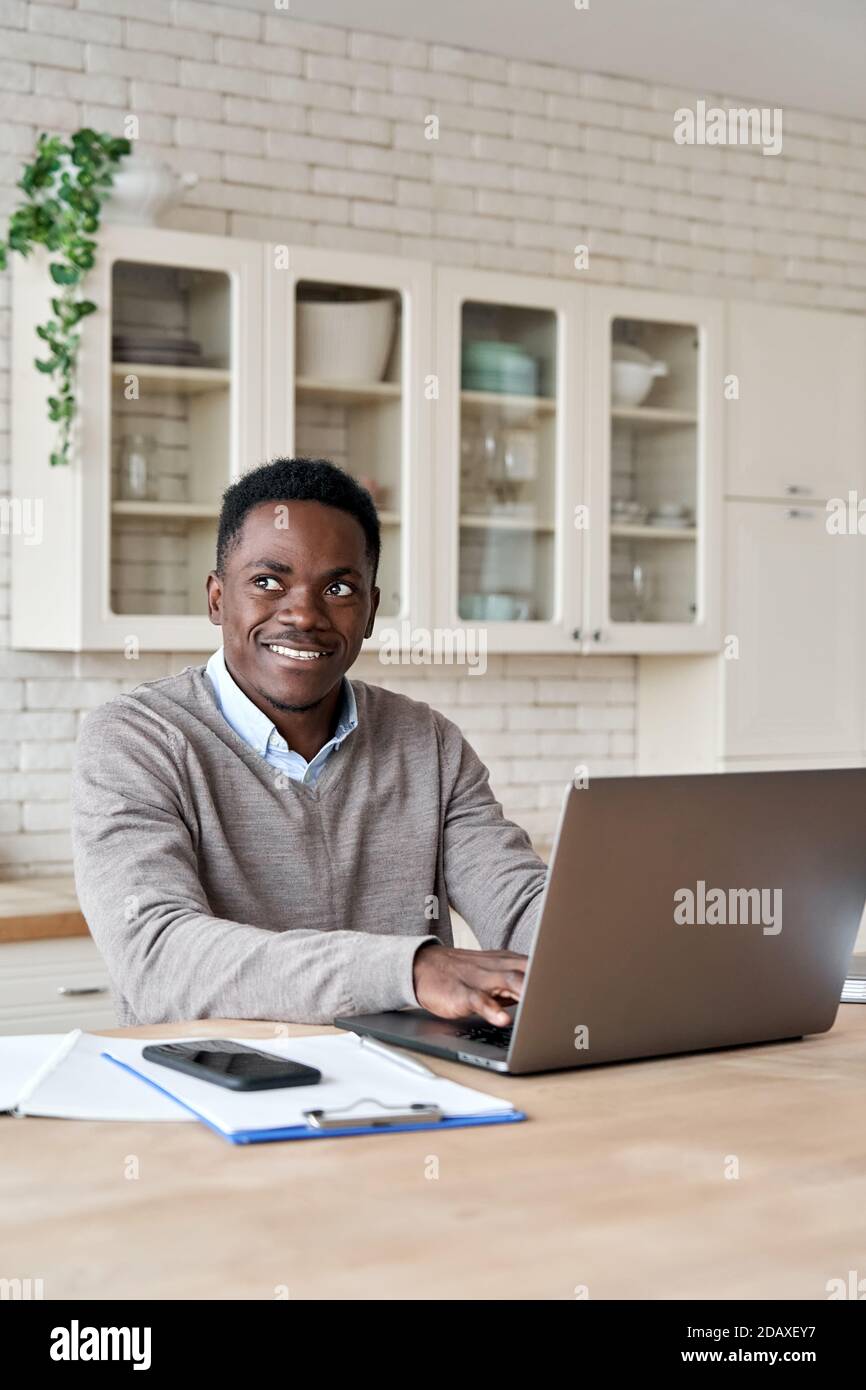 Smiling african american man using laptop working from home office, vertical. Stock Photo