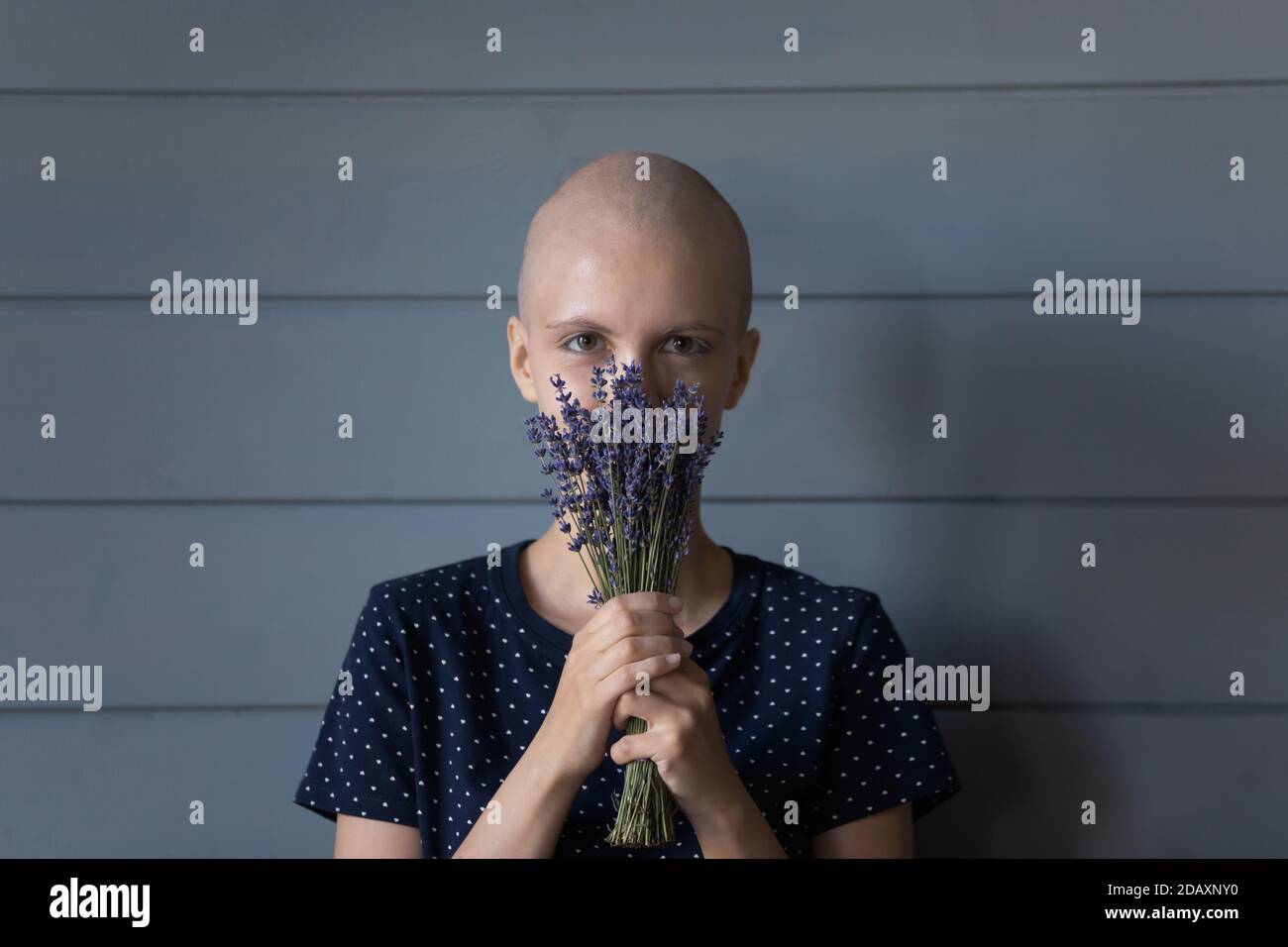 Young hairless woman hiding face in lavender bunch enjoying aroma Stock Photo