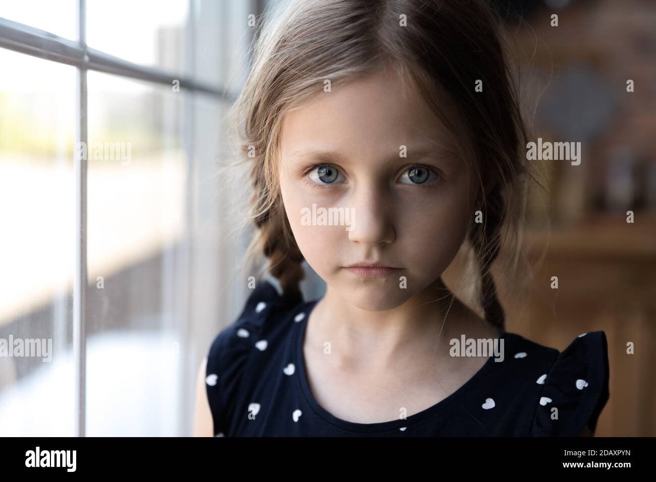 Portrait of serious little school age girl standing by window Stock Photo