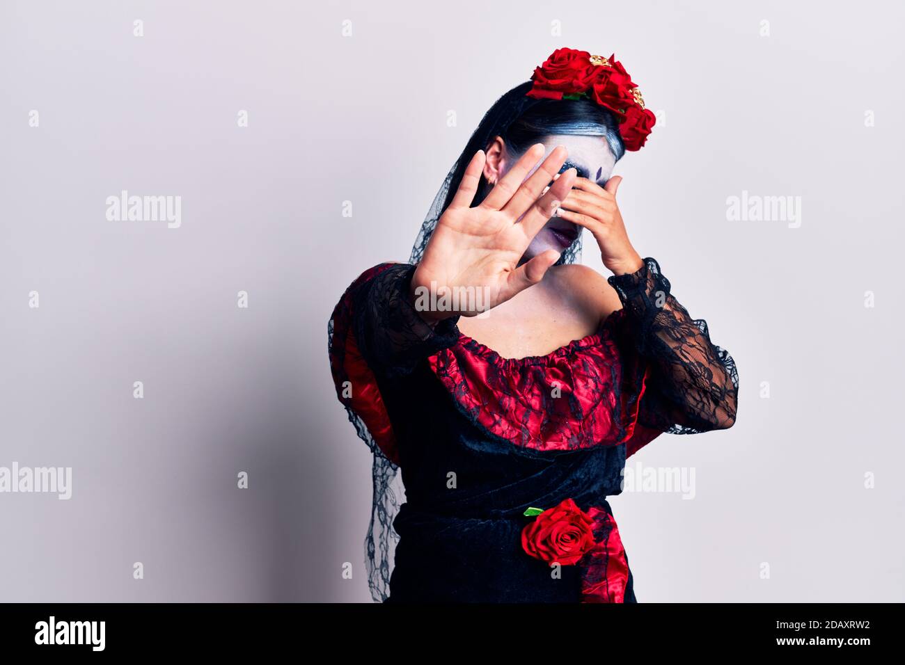 Young woman wearing mexican day of the dead makeup covering eyes with hands and doing stop gesture with sad and fear expression. embarrassed and negat Stock Photo