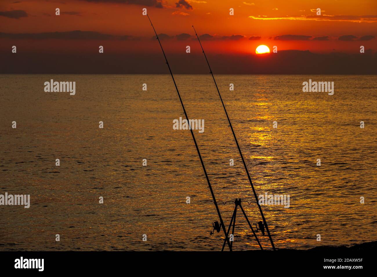 front view of the sea sunset in the foreground two fishing rods and in the background the sea and the setting sun Stock Photo