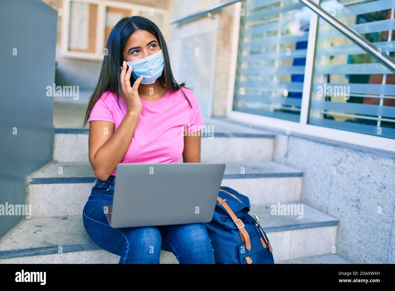 Young latin student girl wearing medical mask talking on the smartphone ...