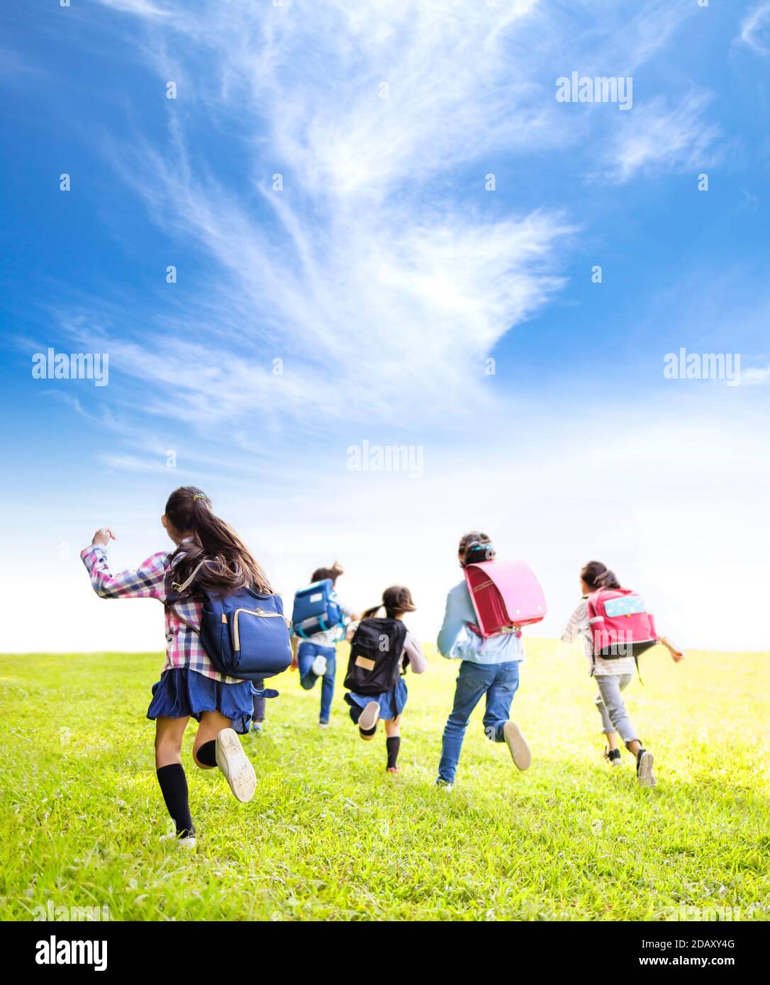 rear view of elementary school kids running on the grass Stock Photo