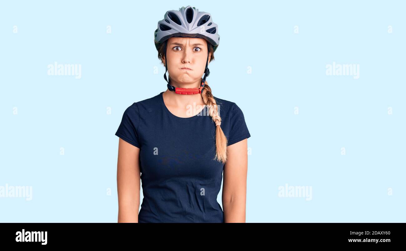 Beautiful caucasian woman wearing bike helmet puffing cheeks with funny