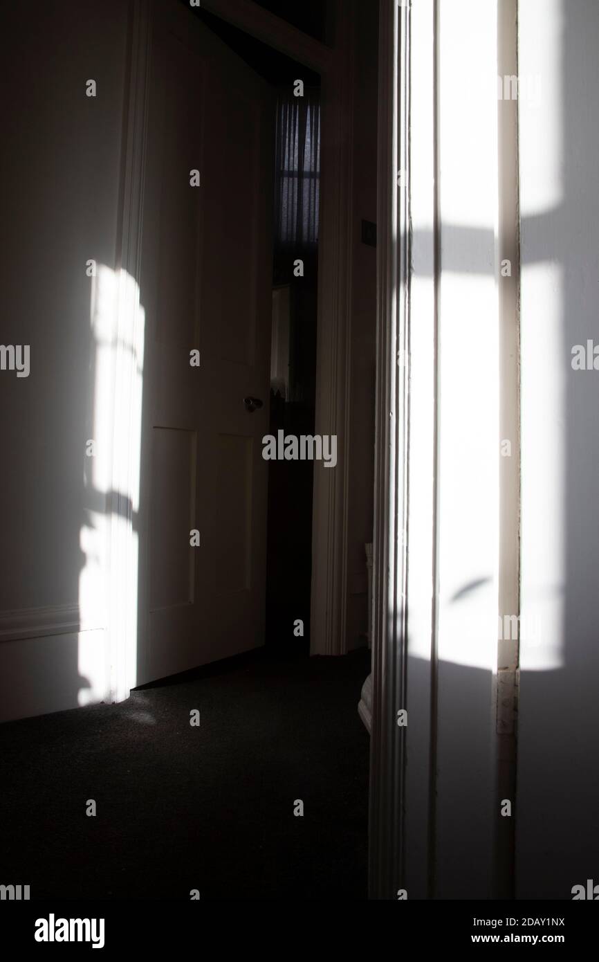 Corridor with contrasting light and shade leading to door ajar and a