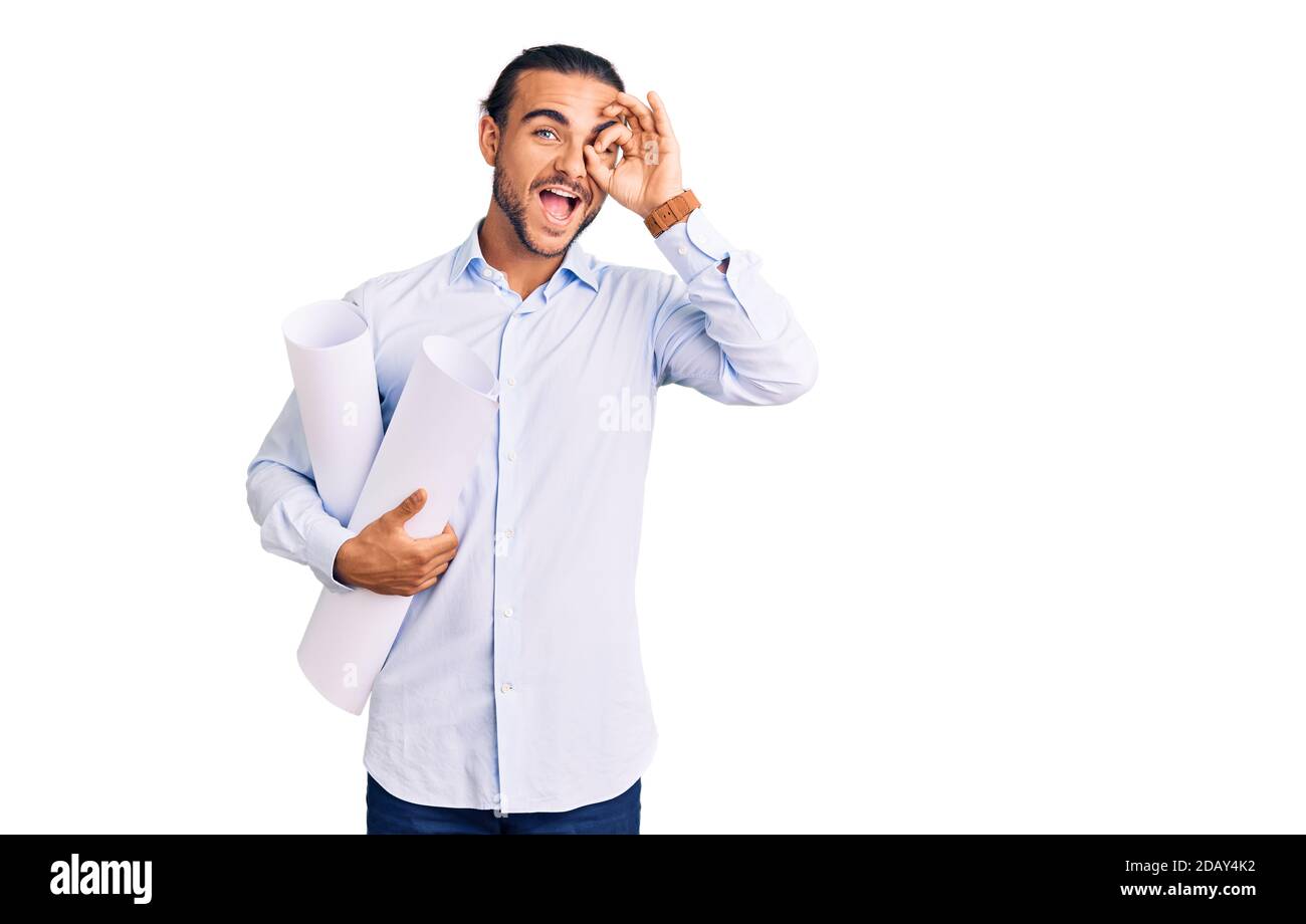 Young handsome man holding paper blueprints smiling happy doing ok sign with hand on eye looking through fingers Stock Photo