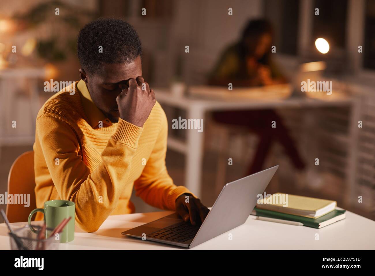 Portrait of exhausted African-American man rubbing eyes while working late at night in dark office, copy space Stock Photo