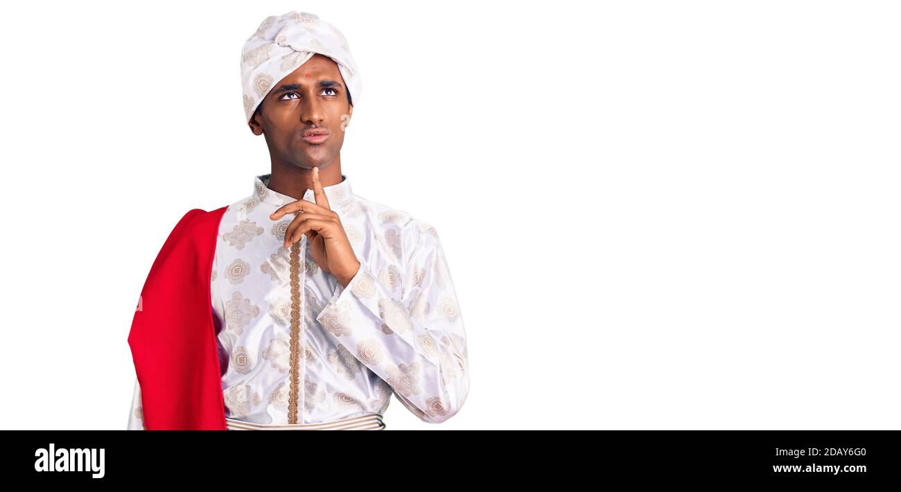 African handsome man wearing tradition sherwani saree clothes thinking concentrated about doubt with finger on chin and looking up wondering Stock Photo