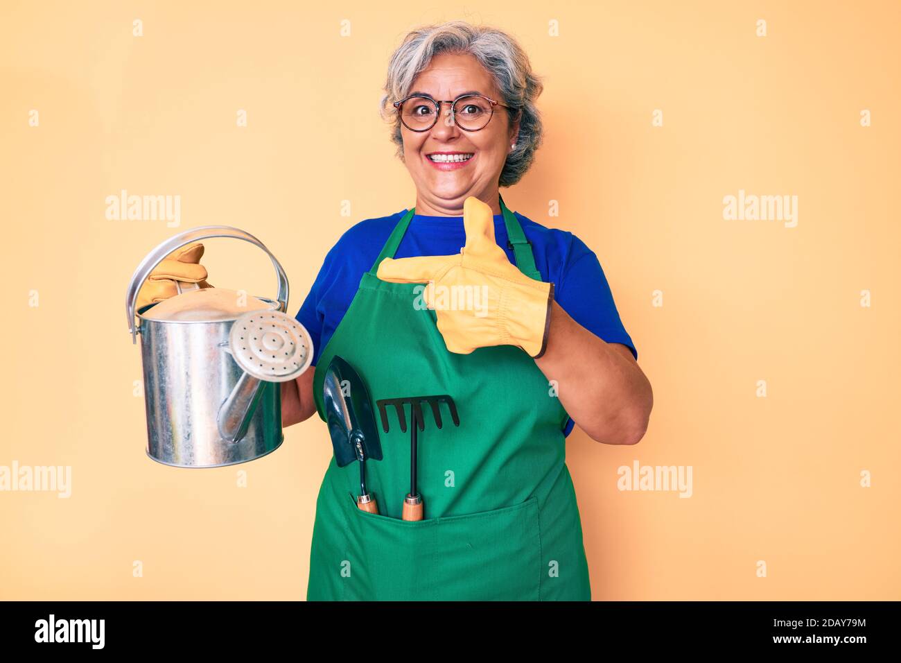 Senior hispanic grey- haired woman wearing gardener apron and gloves ...