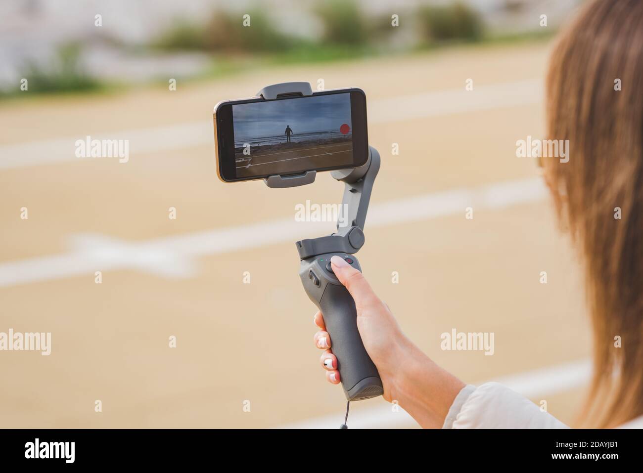 Woman hand holding gimbal with phone. Taking pictures and live video near the ocean. Vlog and video blogging concept. Stock Photo