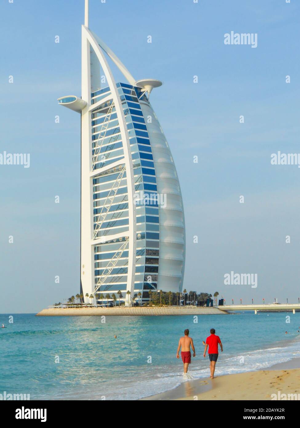 Two men stroll on the beach in front of the Burj Al Arab building in Dubai UAE Stock Photo