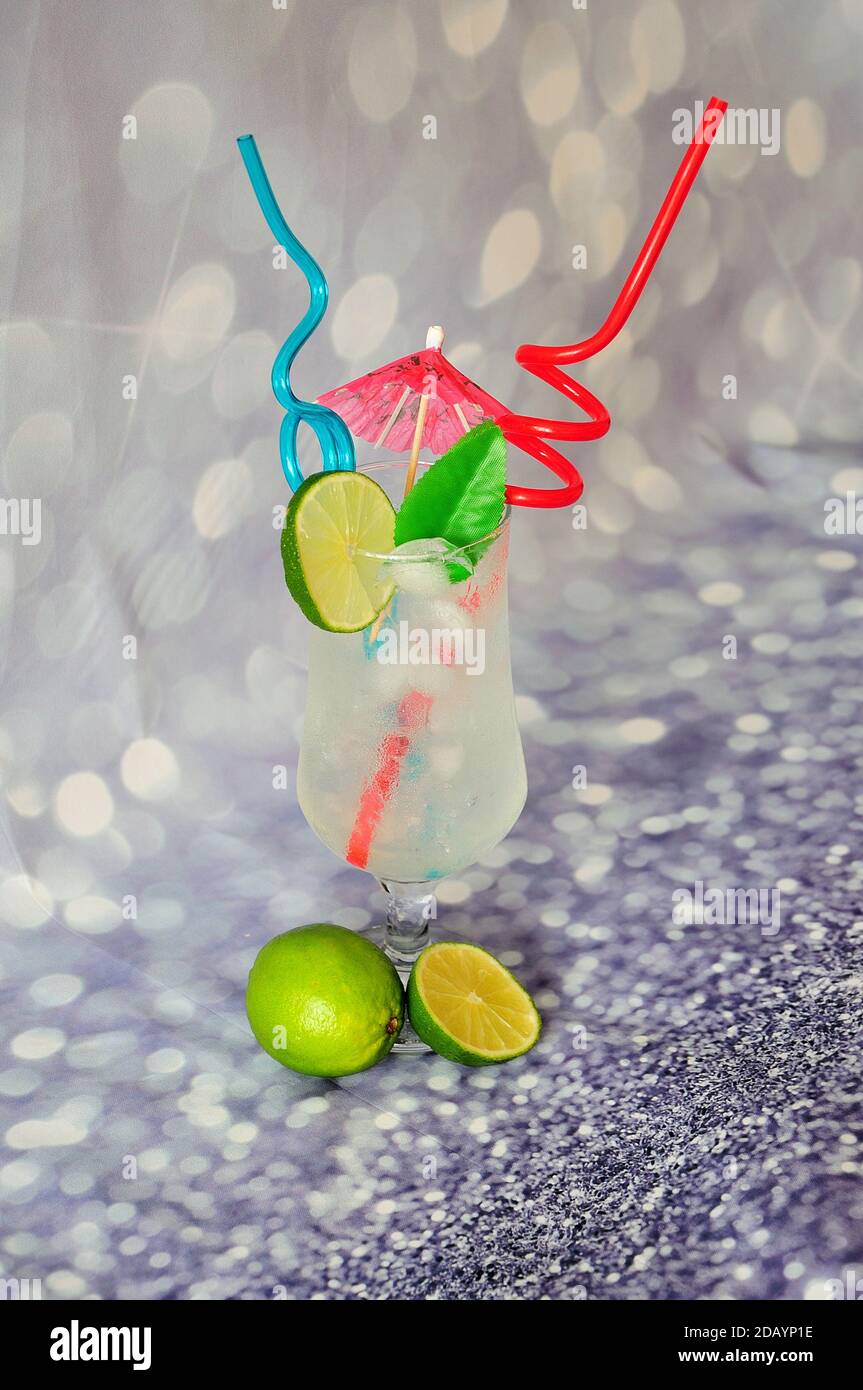 A tall glass of lime juice with ice and a slice of citrus with straws ...