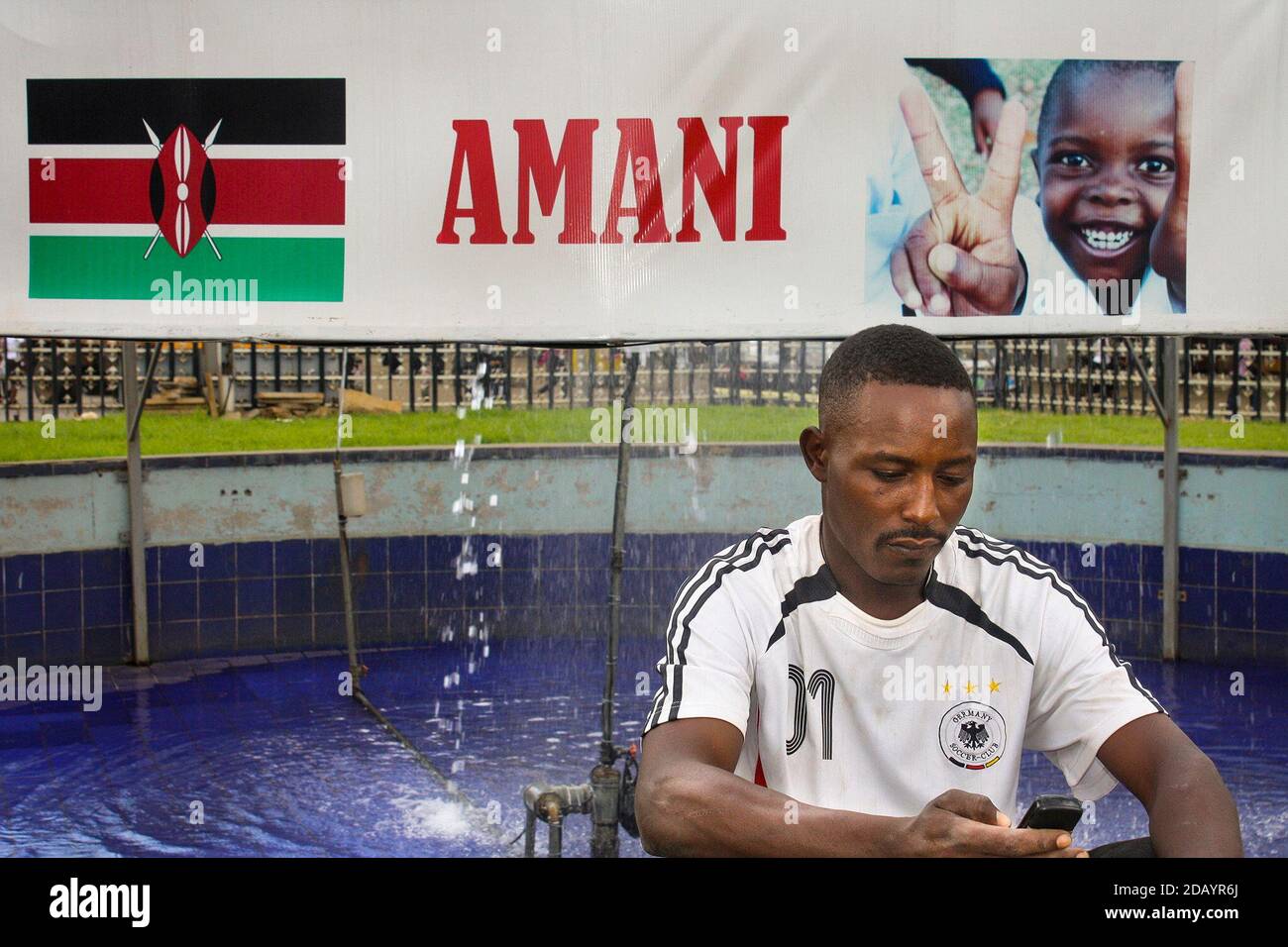 Fred Manundu uses his mobile phone to browse the Internet in front of a peace banner in Nairobi. Stock Photo