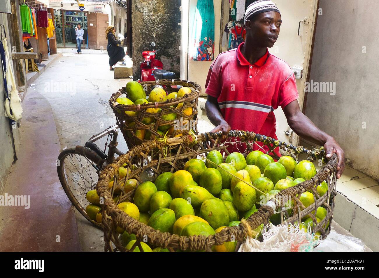 A traveling merchant sells fruit door-to-door in Stone Town, a historic section of Zanzibar town on the island of Zanzibar, which is part of Tanzania. Stock Photo