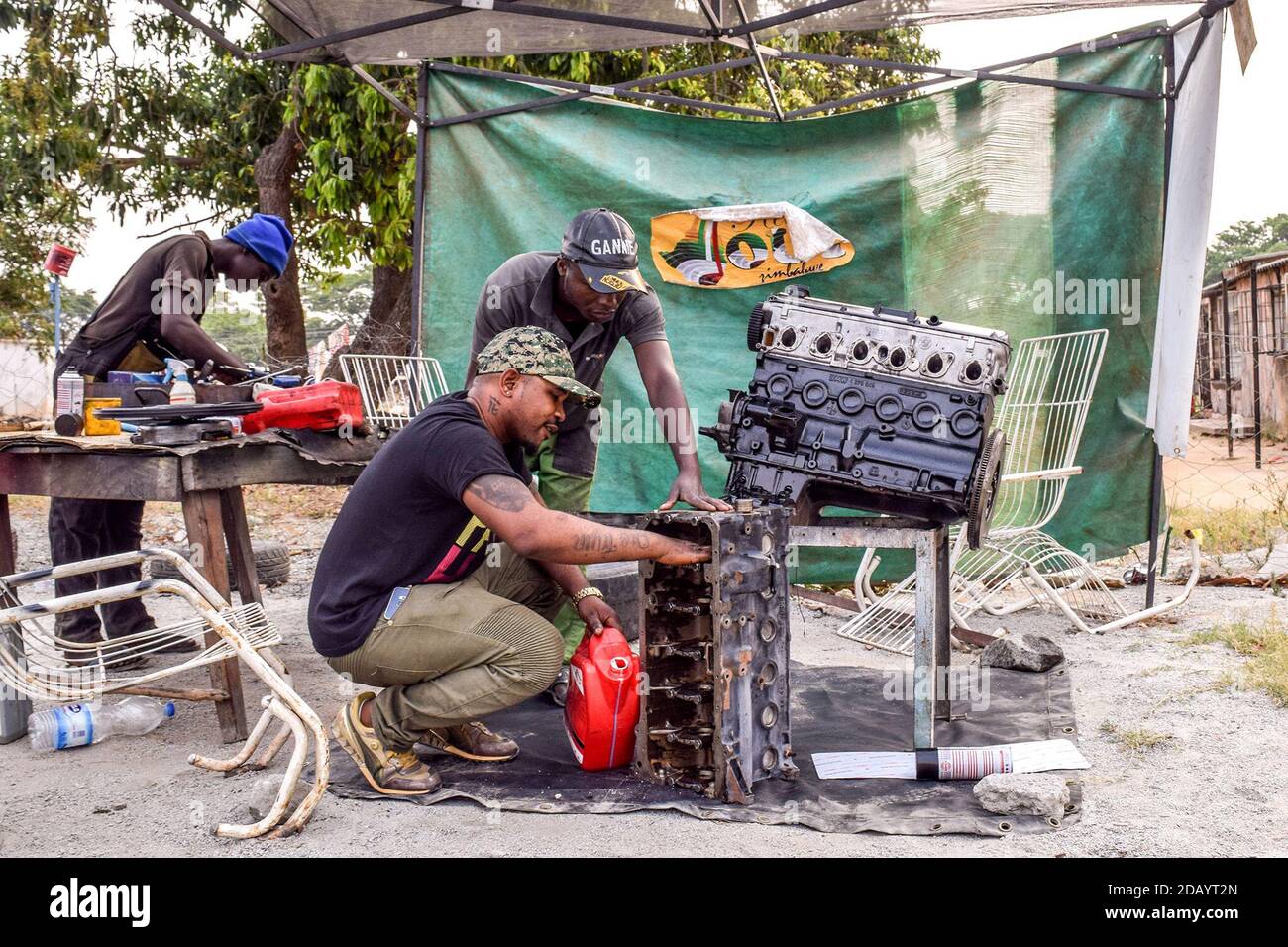 Rusell Chirindo, who's spinning name is Cici Boy, and Andrew Wandikani (center) smear oil on an engine block to protect it from rust. Stock Photo