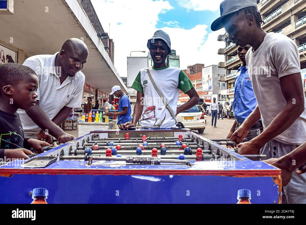 Divine Kaliofasi (left), 7, plays table football, locally known as 'slug,' with bus drivers and conductors at the commuter park in Harare, Zimbabwe. Stock Photo